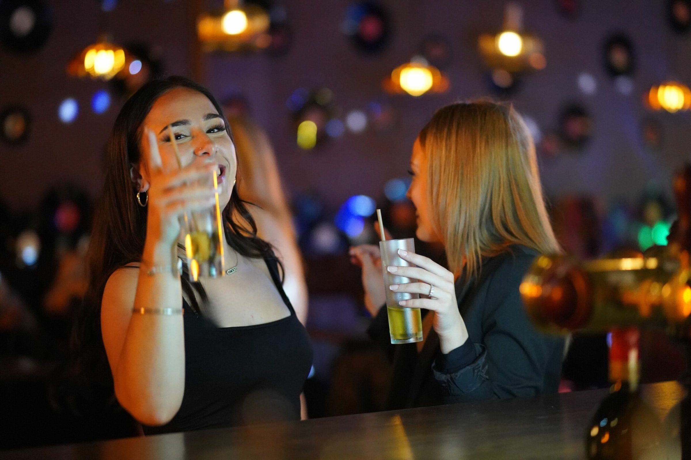 Deux amies trinquent au comptoir de l’Old Fashioned, cocktails à la main, vinyles au mur